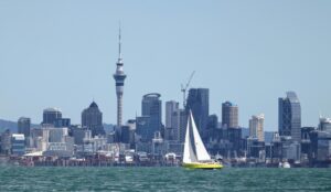 A yellow sailboat in the ocean with the city line in the background.